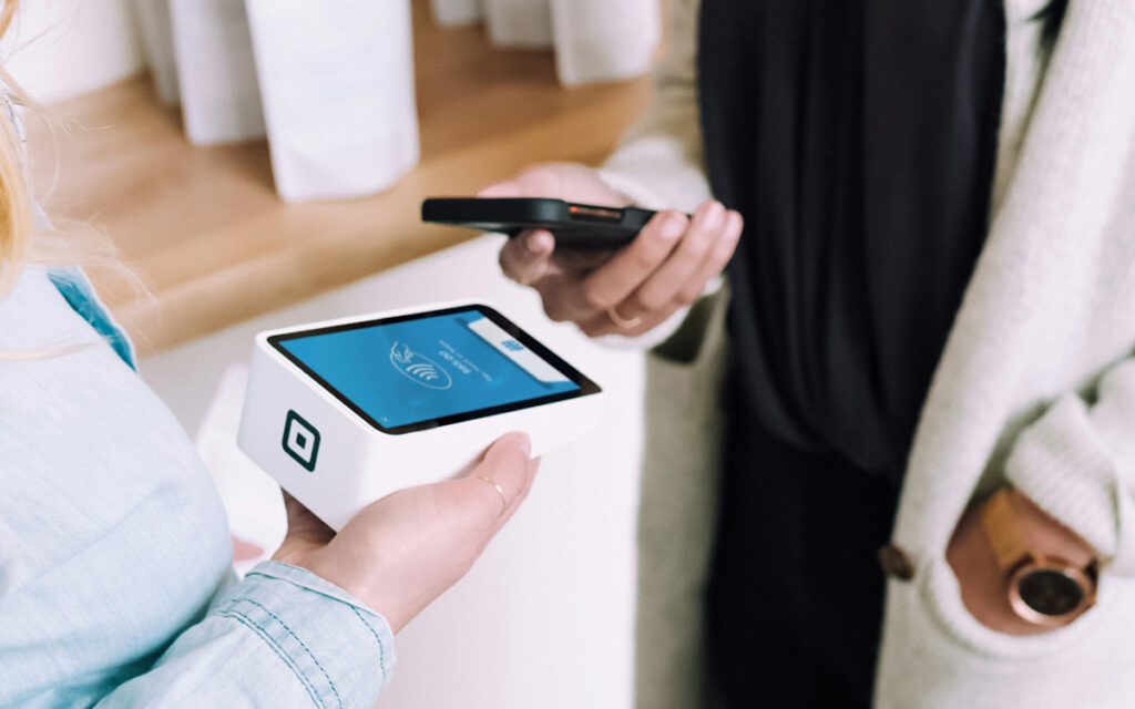 A photo of two people processing a payment using a mobile point of sale terminal and a cell phone.