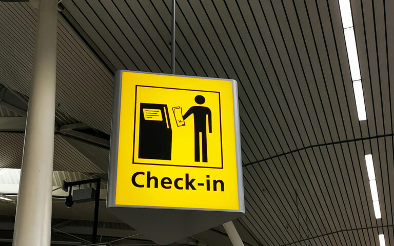 Photo of a yellow and black sign at an airport or train station indicating where to find the check in desk